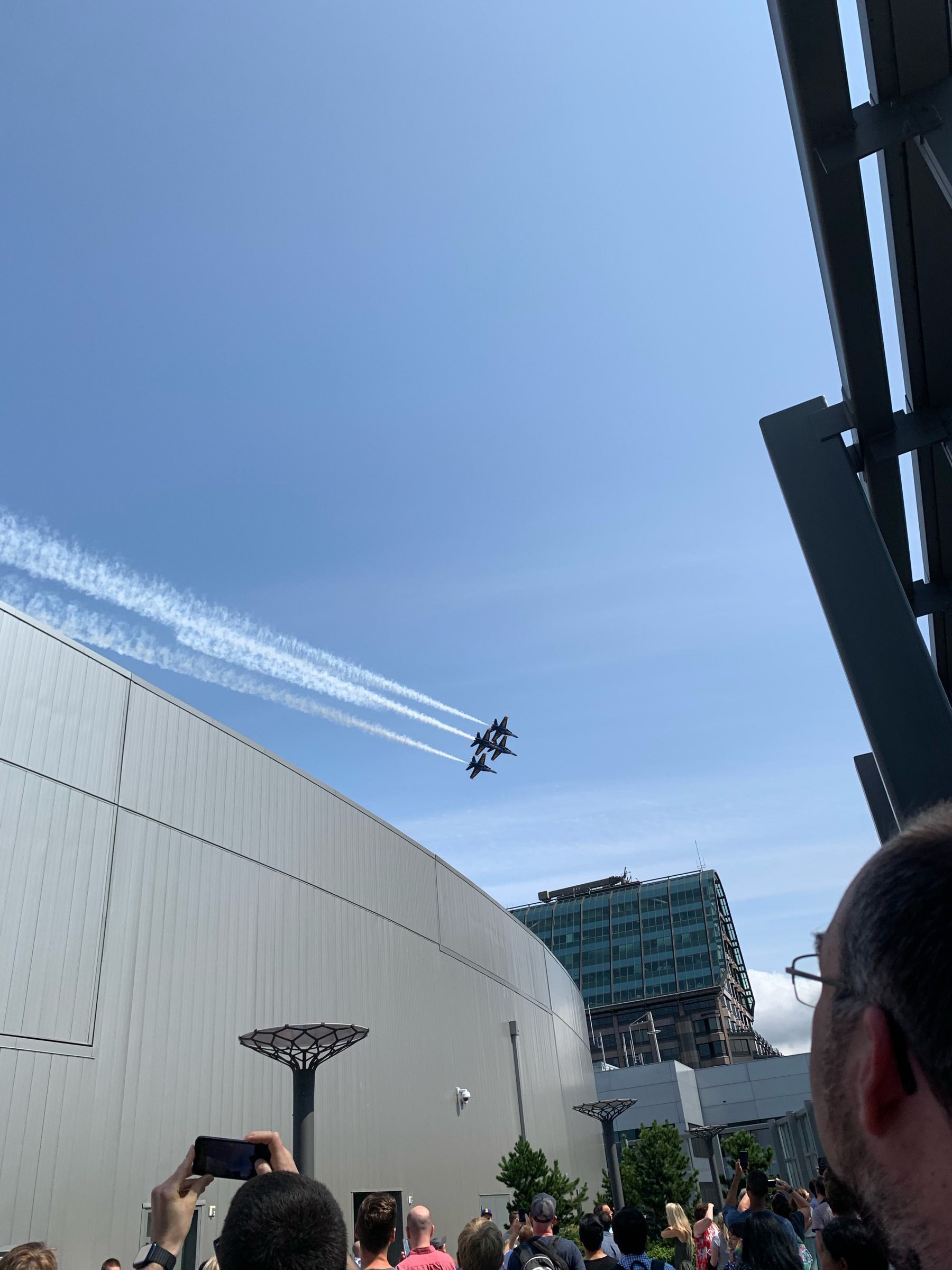 Four military aircraft flying in close formation as seen from a crowded rooftop.